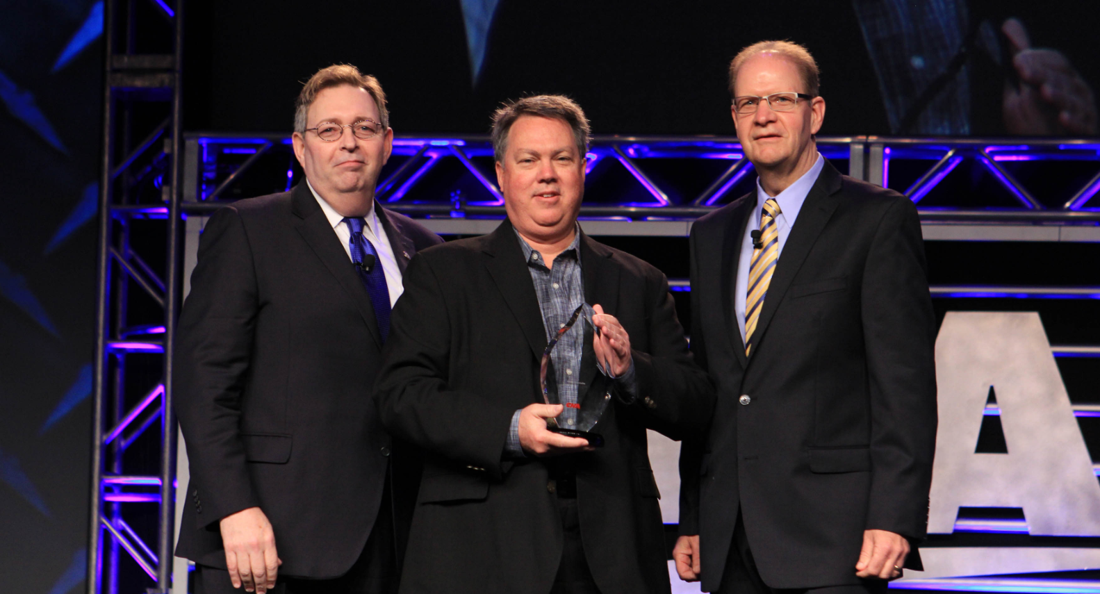 three men in suits holding a glass award for safety